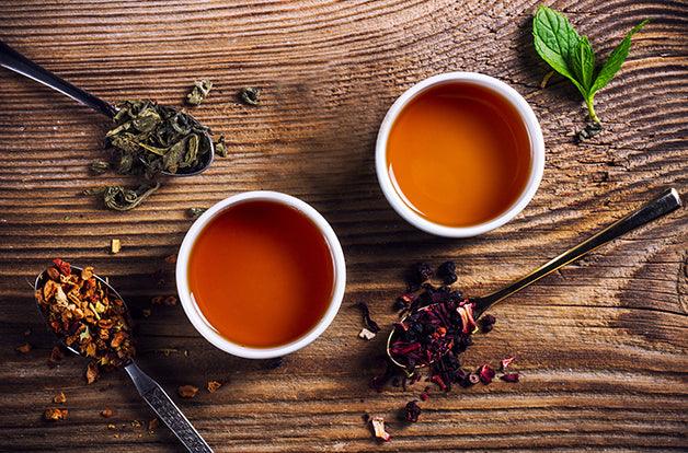 Two cups of loose leaf tea on a wooden table, top view