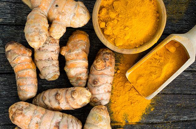 Fresh turmeric roots and turmeric powder on wood background